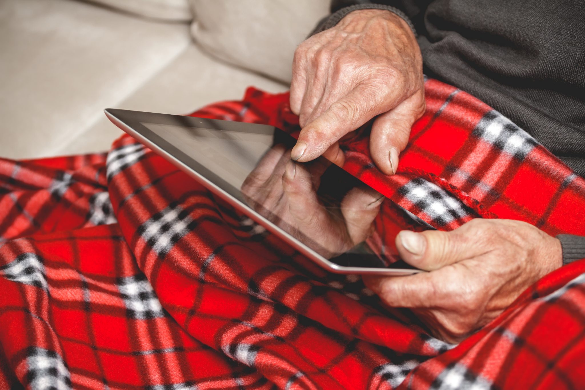 Elderly man sitting on sofa reading tablet computer