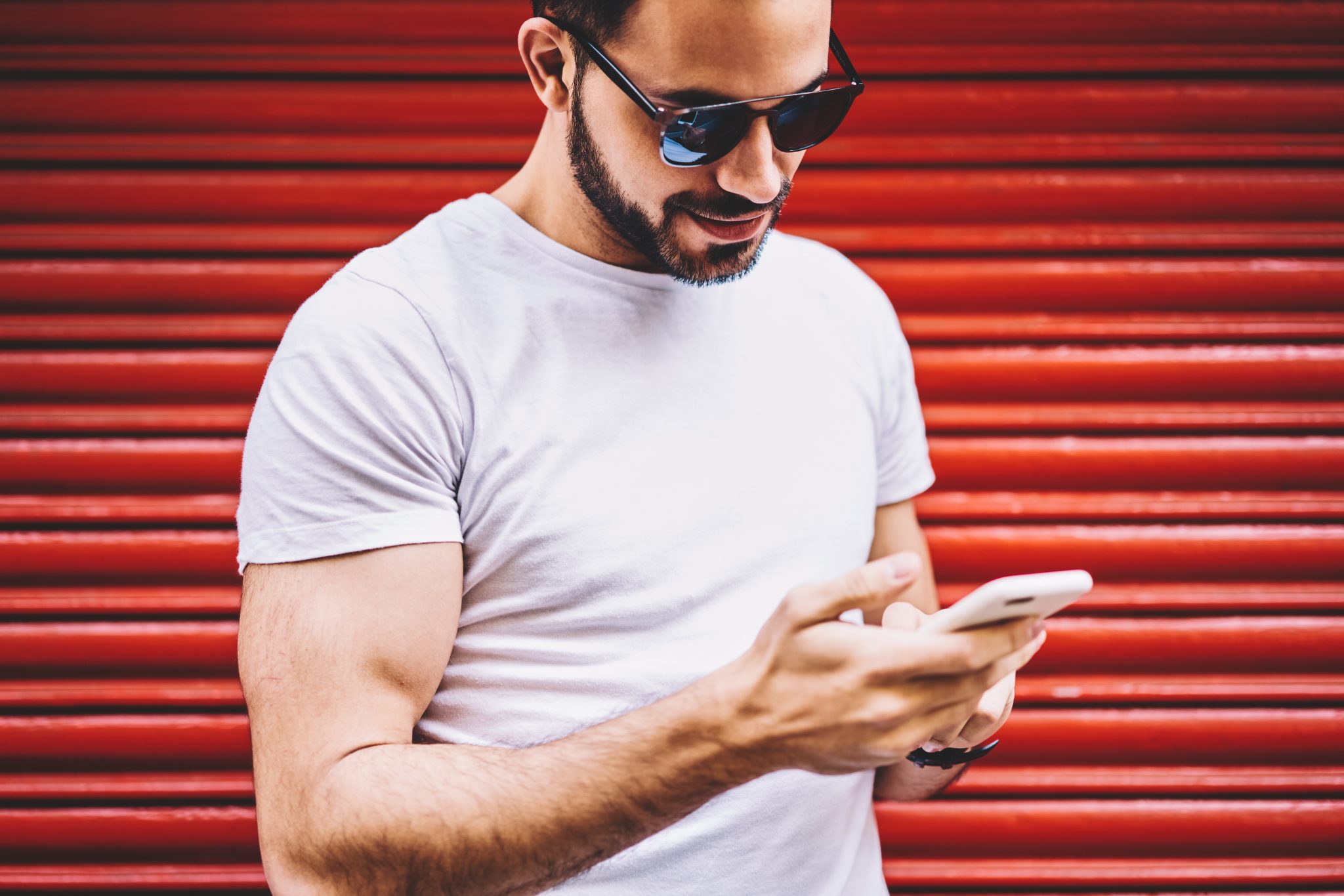 Young man in sunglasses looking at smartphone against red background