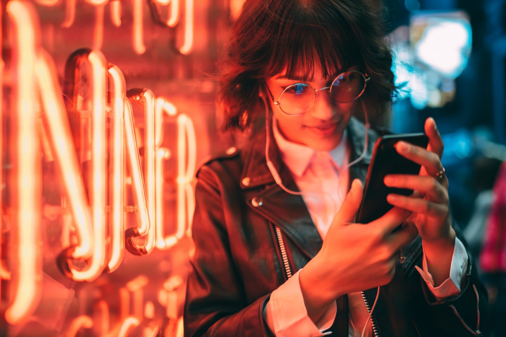 Young woman looking at smartphone next to red neon light