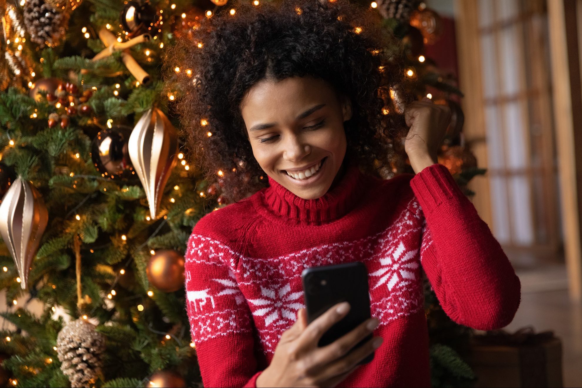 Young woman in red Christmas jumper smiling at smartphone