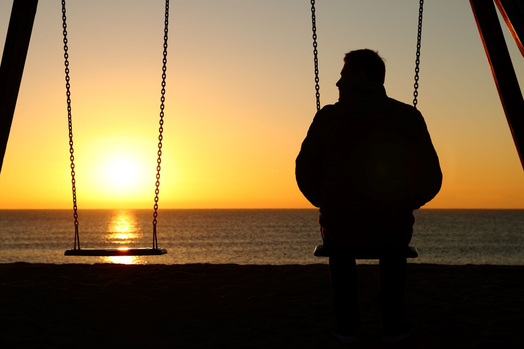 Man sitting on seaside swing at sunset
