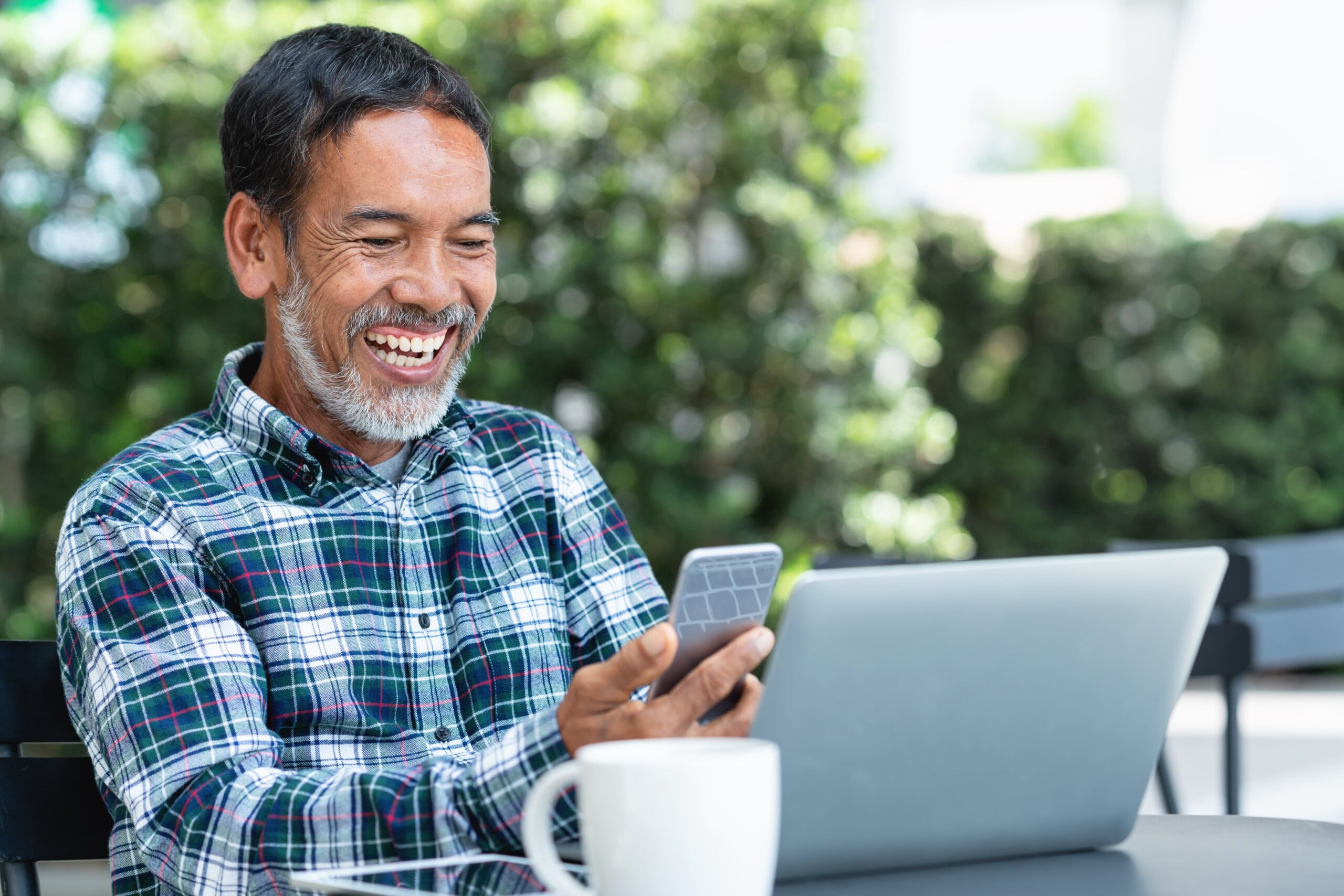 Older smiling man enjoying smartphone and laptop tech