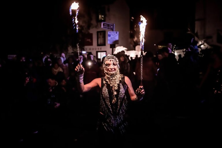 Woman in costume holding flaming torches at night
