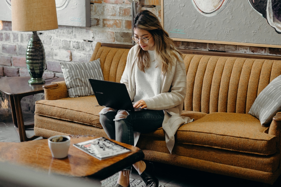 photo of a young woman using a laptop while sitting on a sofa