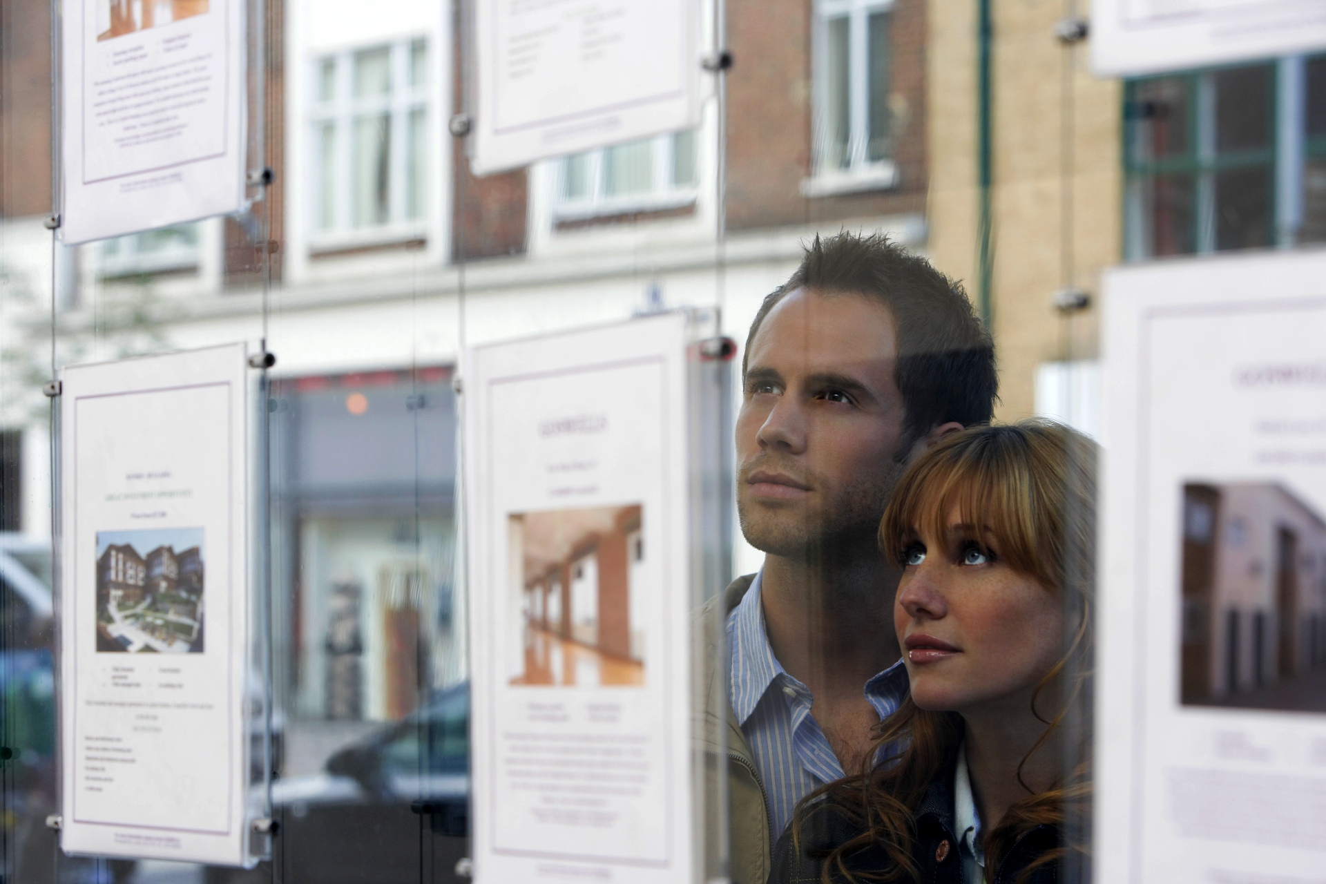 photo of a serious-looking couple reflected in the window of an estate agent office