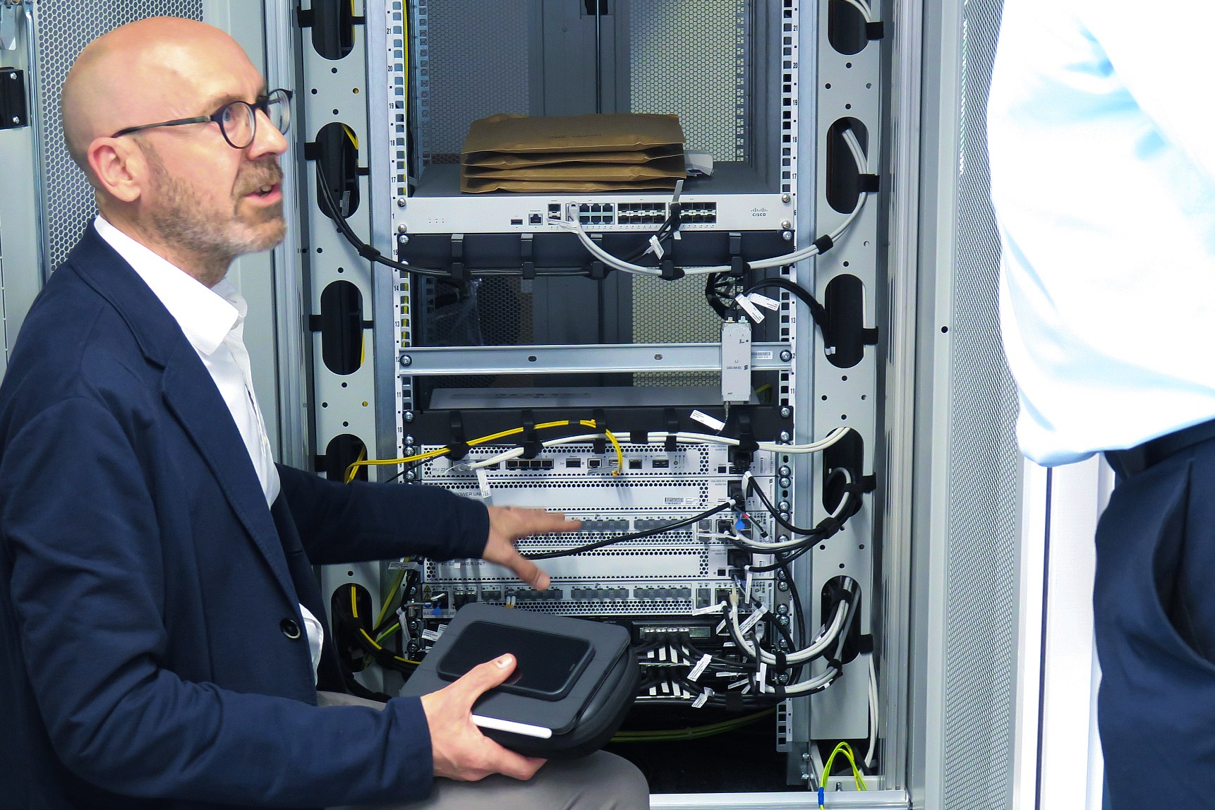 photo of Craig Pemberton, UK Senior Innovation Manager at Vodafone, kneeling down to inspect a server rack cabinet at Uxplore in Coventry while talking to another person just out of shot.