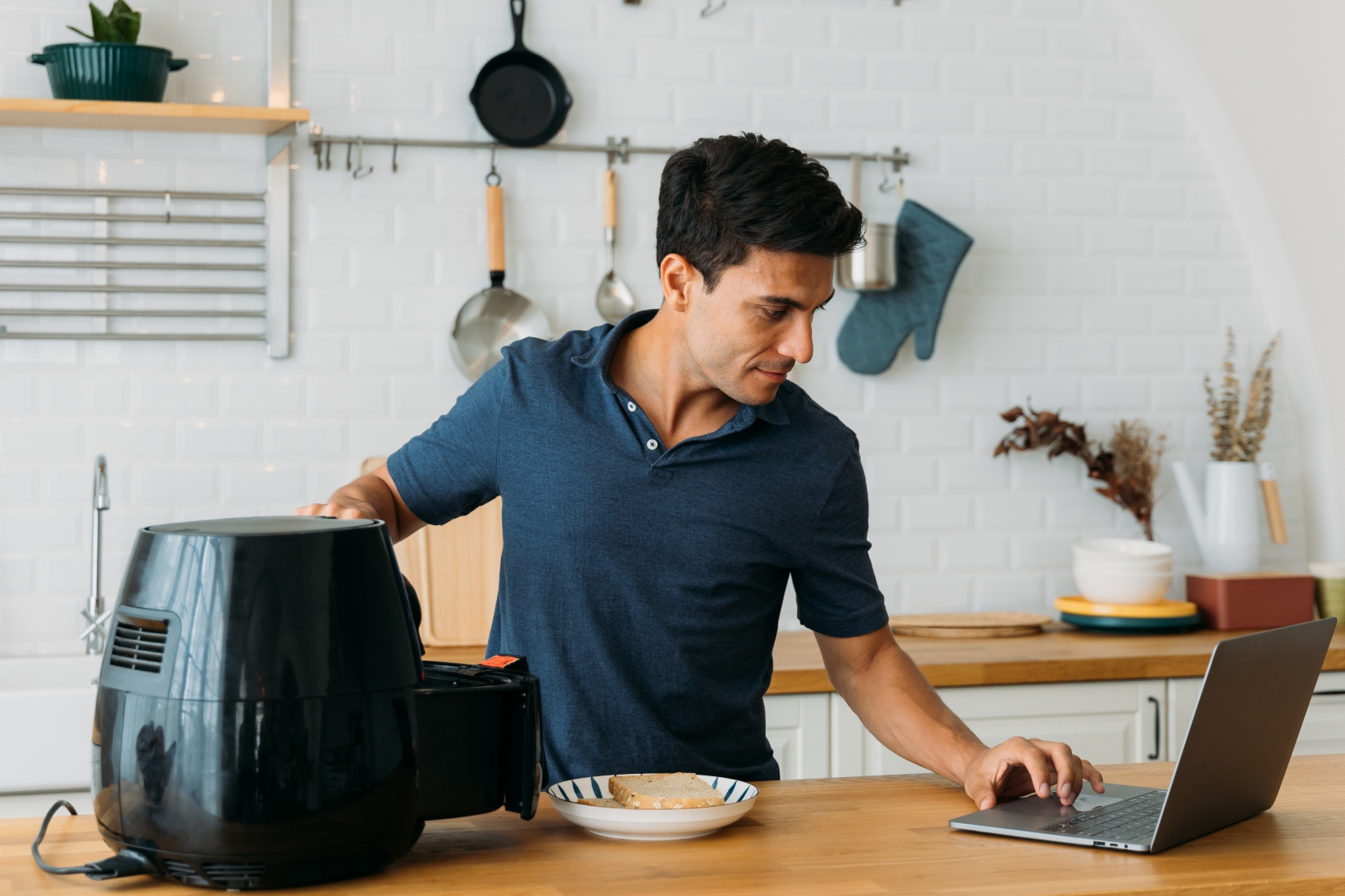 stock photo of a man in a kitchen using a laptop and an air fryer