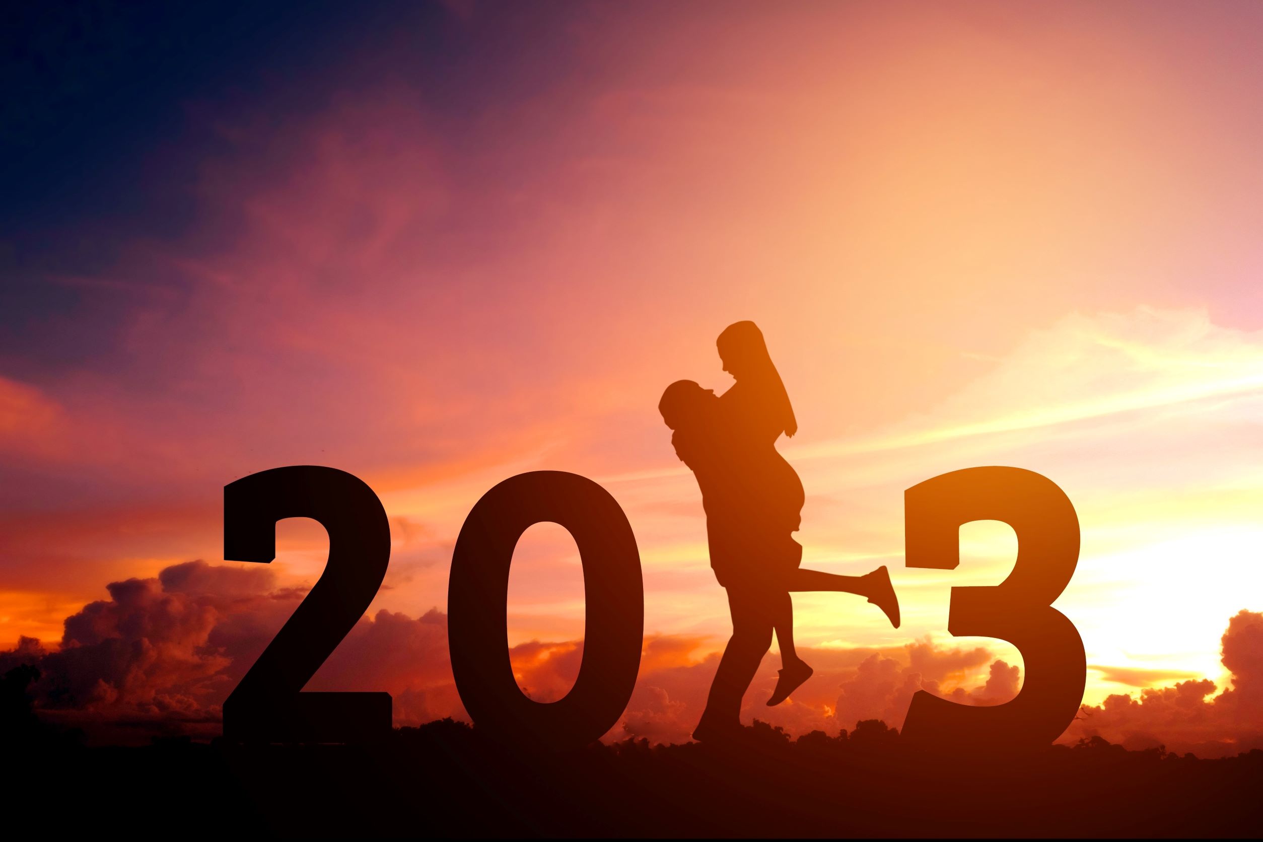 Silhouetted couple within 2023 logo against sunset sky