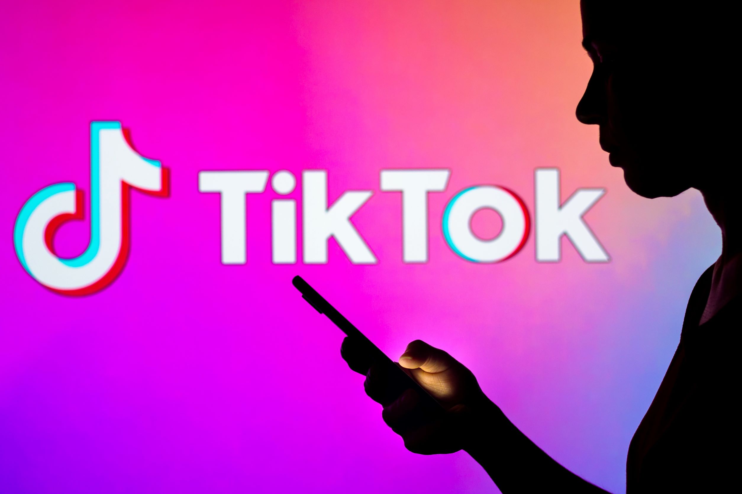 Silhouetted woman reading smartphone in front of TikTok logo
