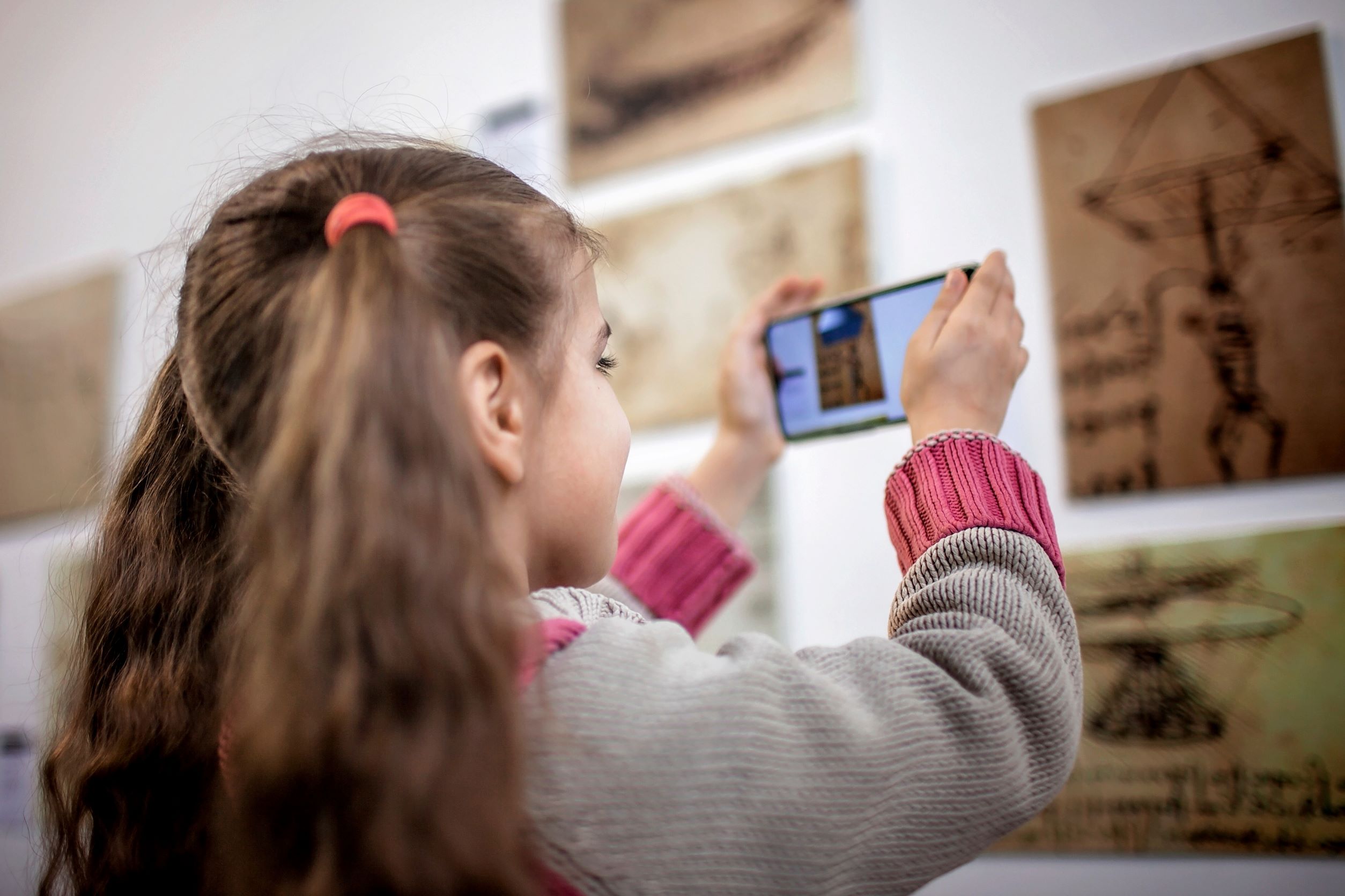 Young girl looking at art in a museum through an AR app on her smartphone