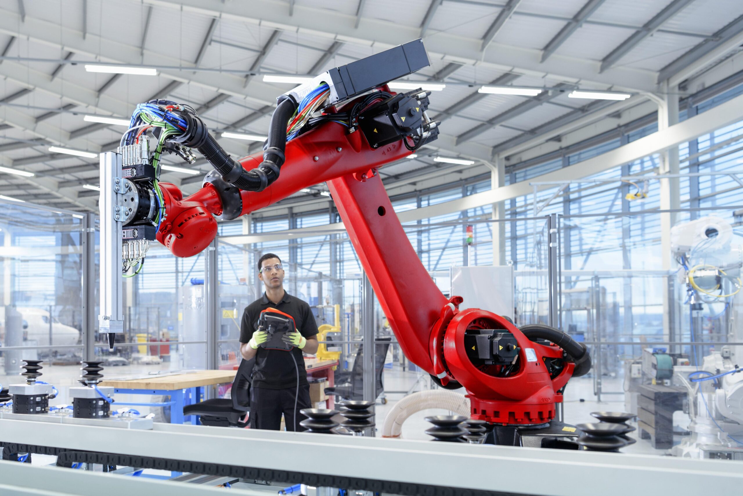 Man remotely operating red precision robot in factory