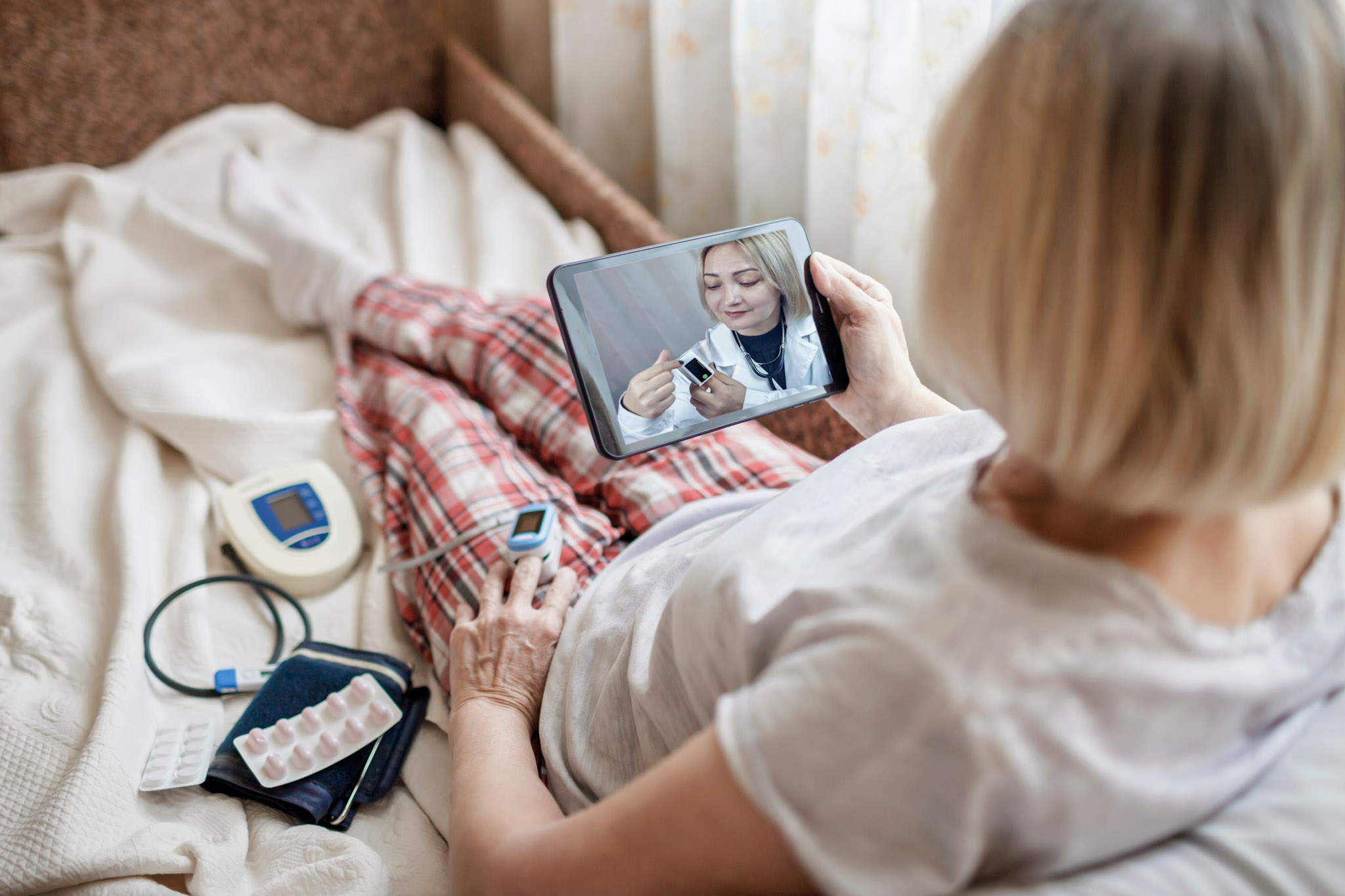 stock photo of an old woman in bed getting a telemedicine appointment on her tablet