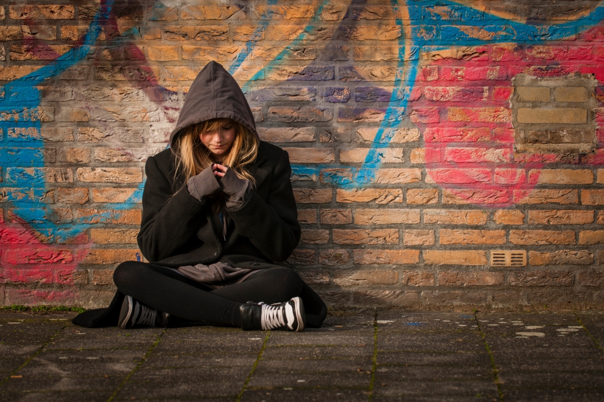 Teenage girl sitting crosslegged against a graffiti-covered wall