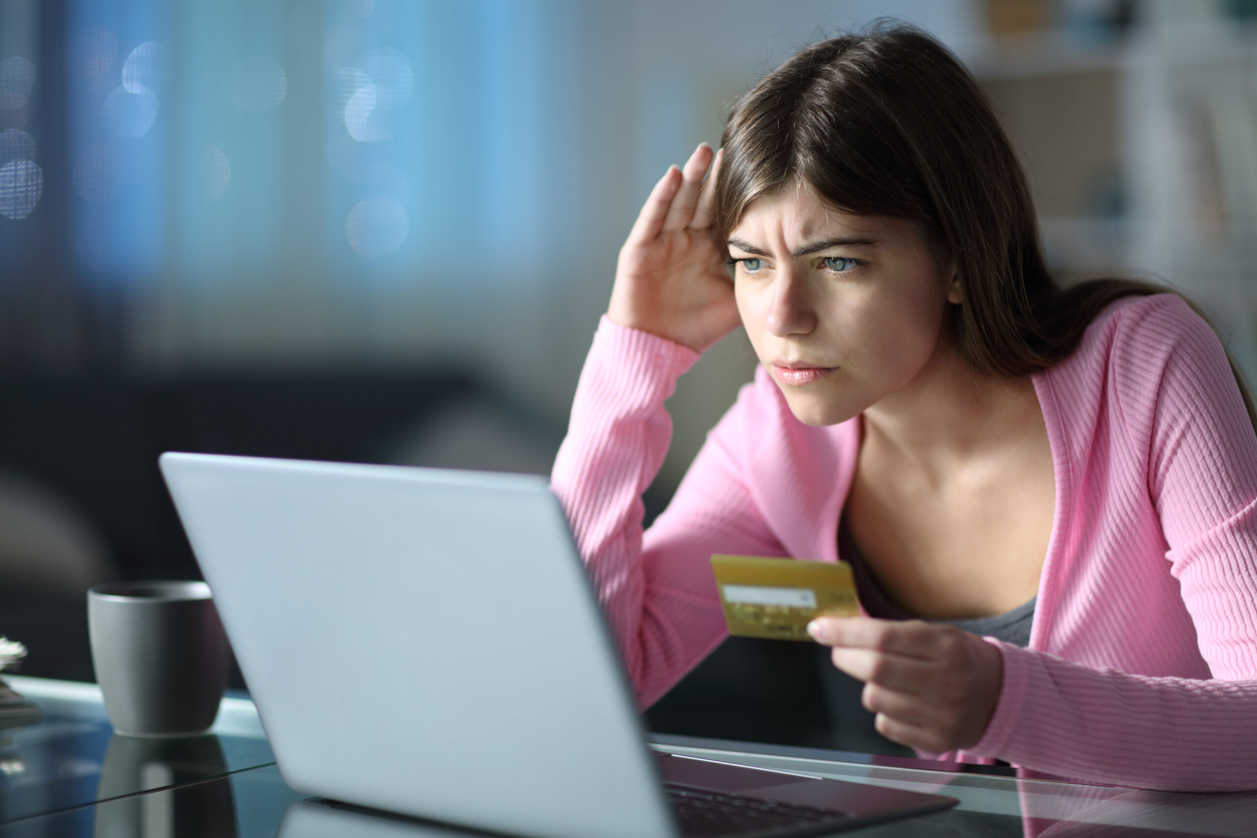 stock image of a worried-looking teenage girl sitting in front of a laptop while holding a credit card