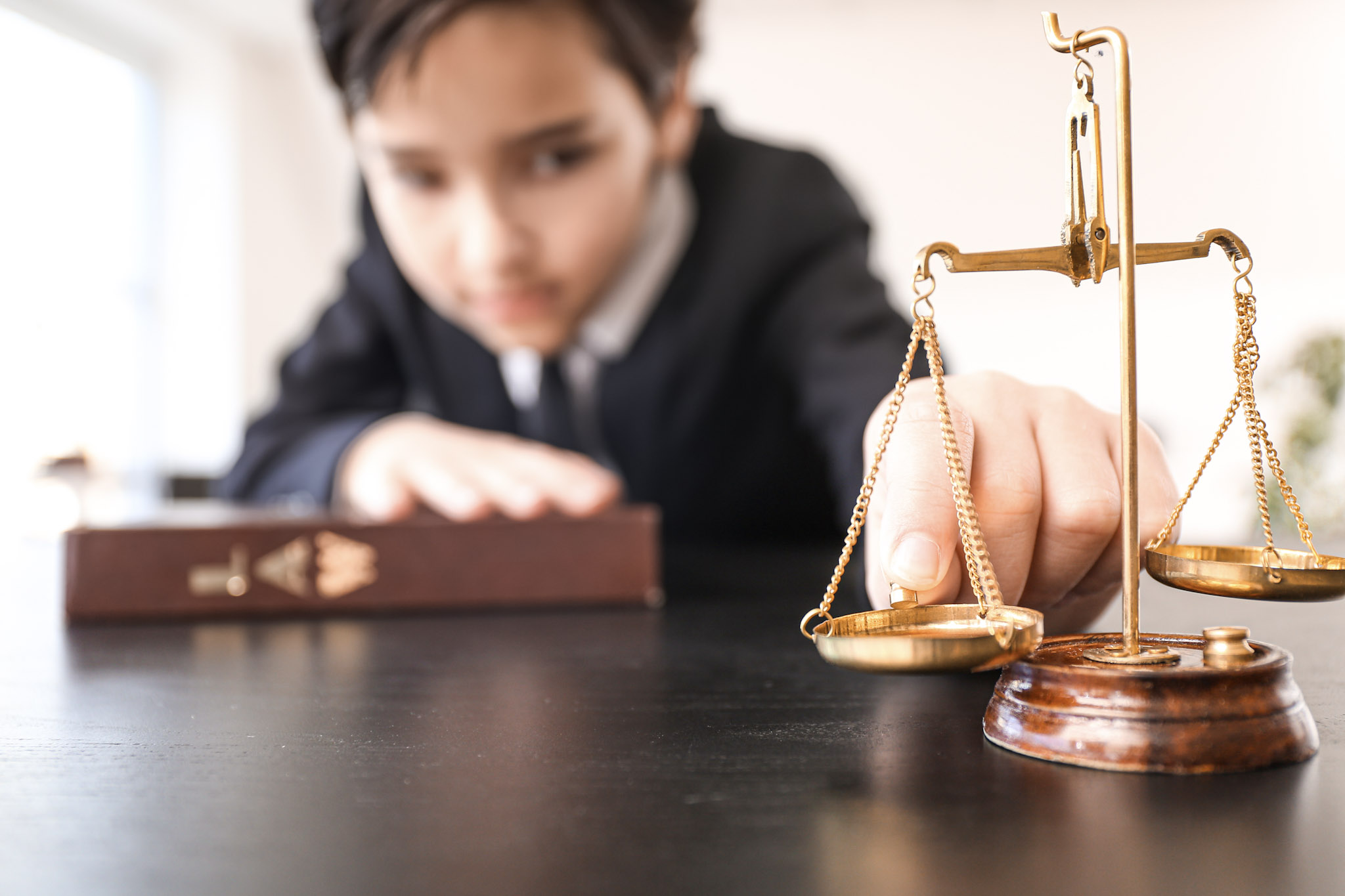 stock photo of a child dressed as a lawyer putting a weight on a model of the scales of justice