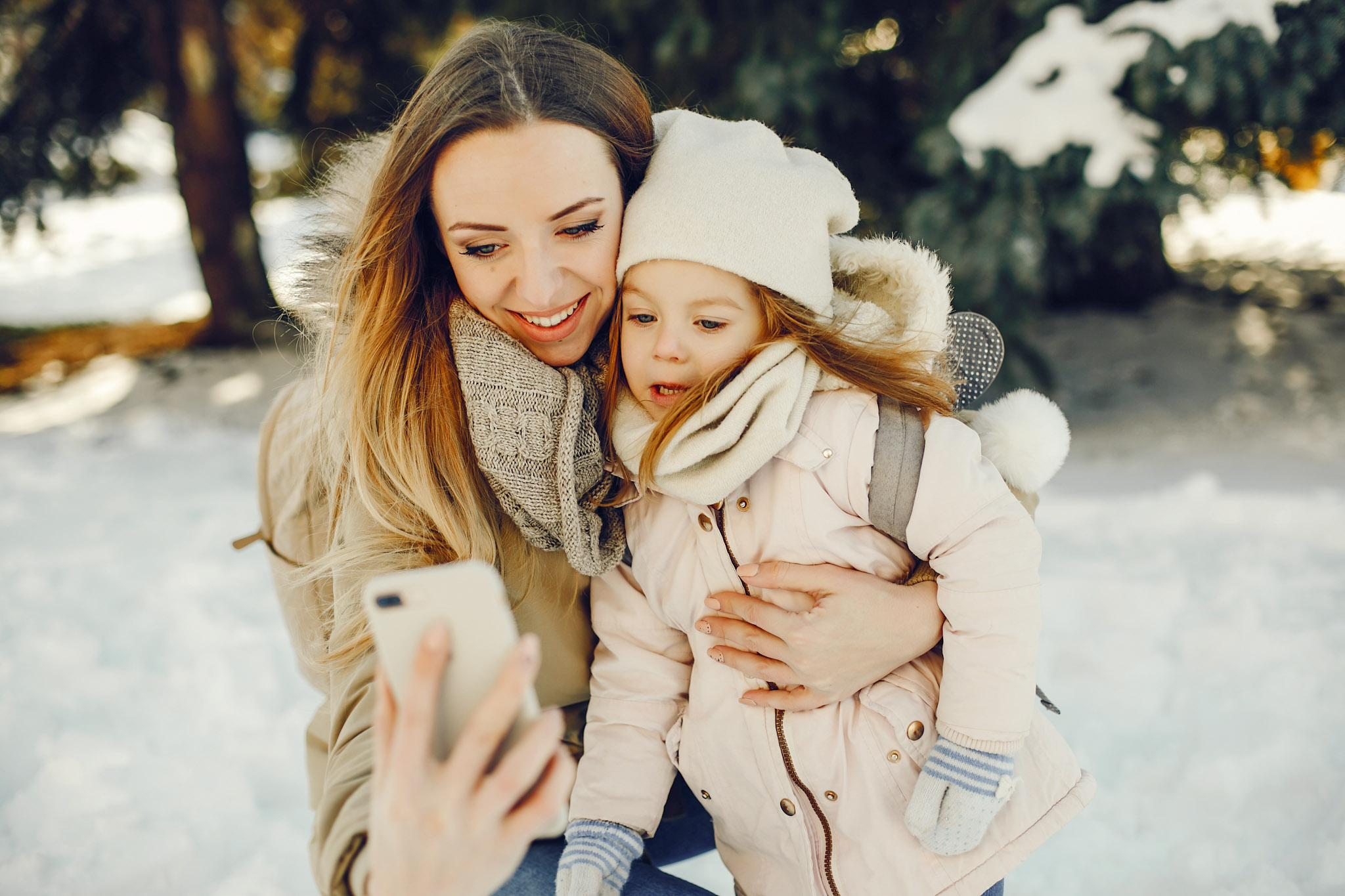 stock photo of a mother outside in snowy weather with her daughter while using a smartphone