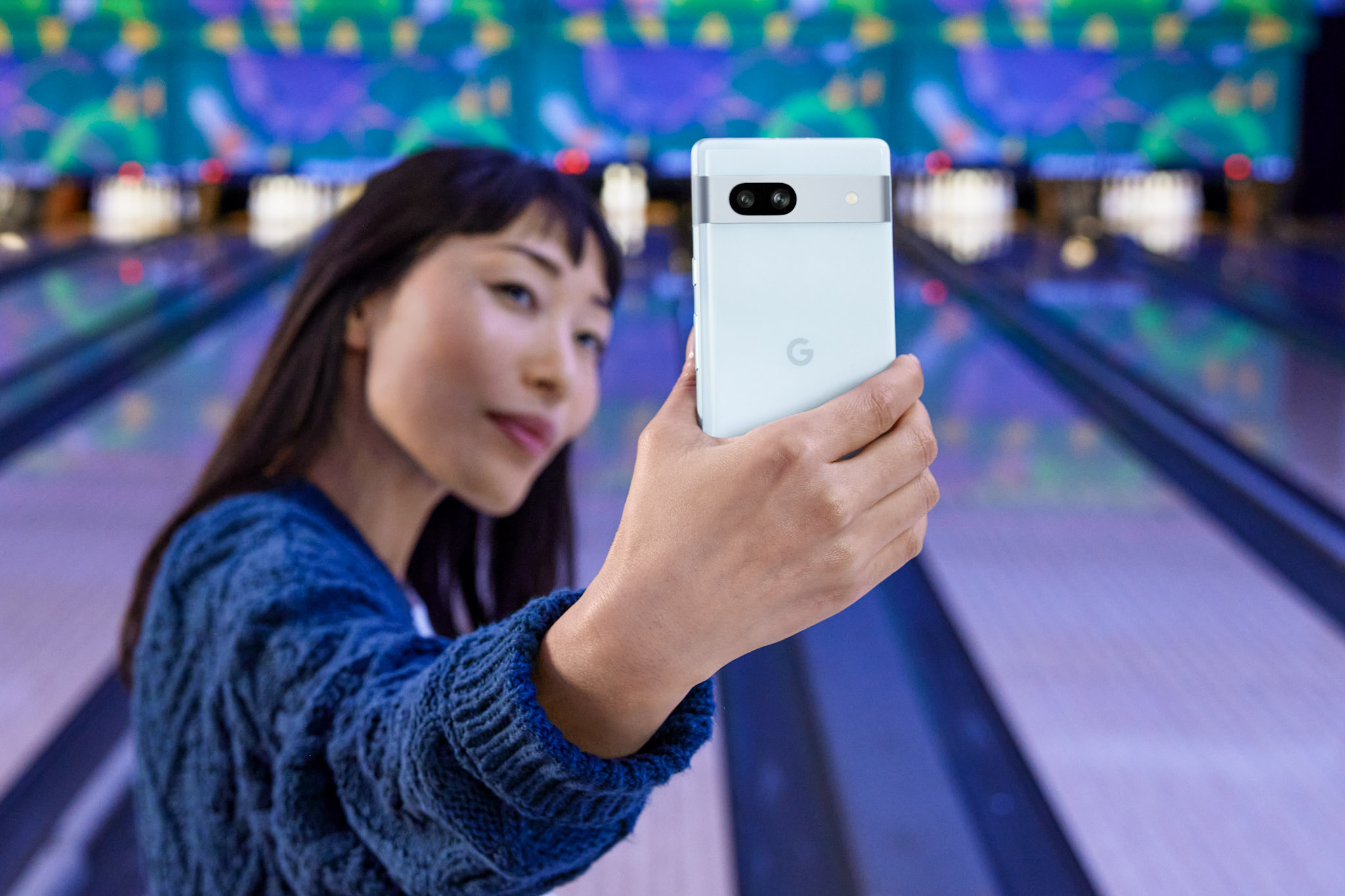 image of a young women taking a selfie in front of a colourful bowling alley using the Google Pixel 7a Android smartphone