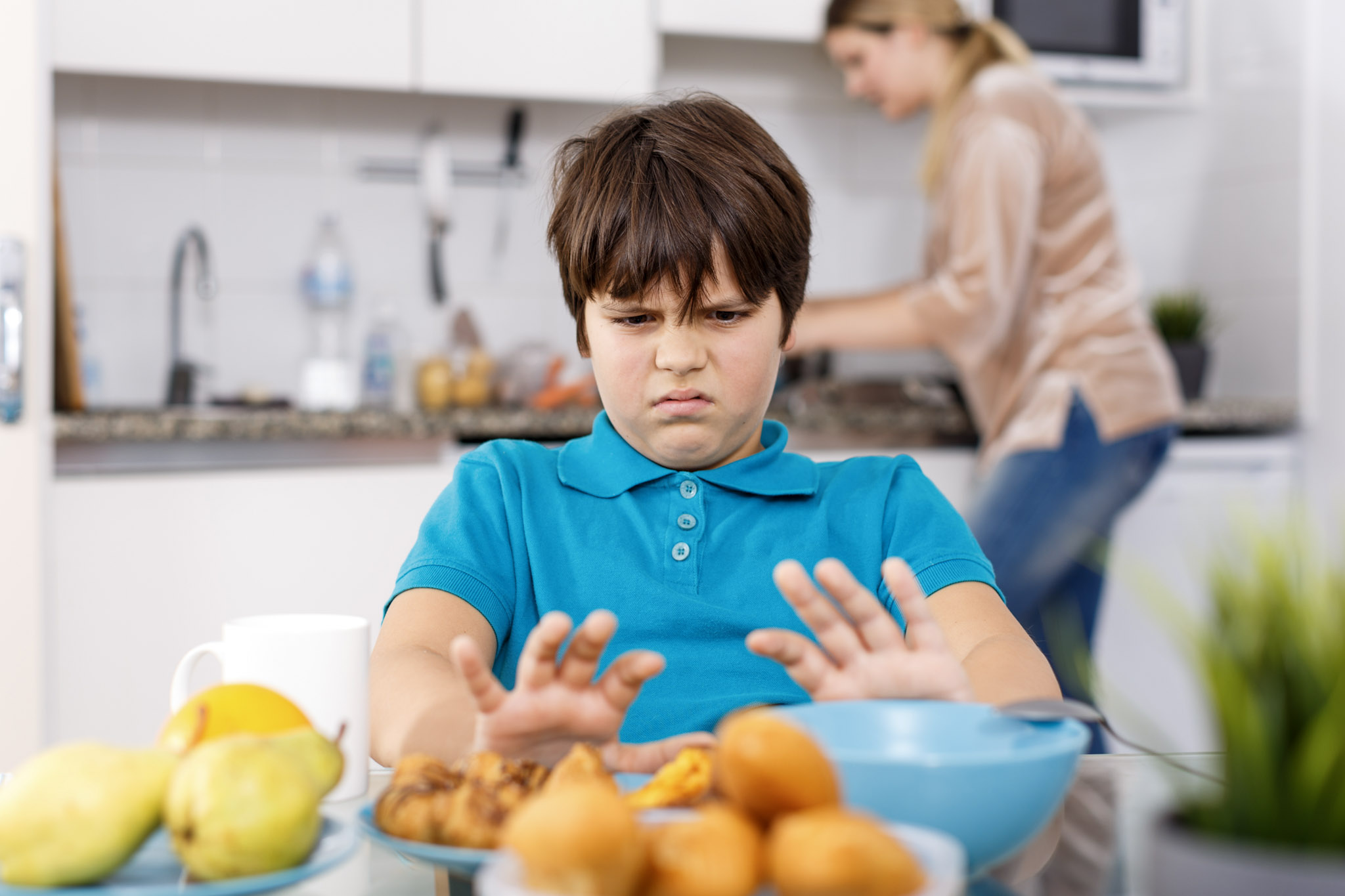 stock photo of a young boy sitting at a kitchen table, refusing to eat the food in front of him