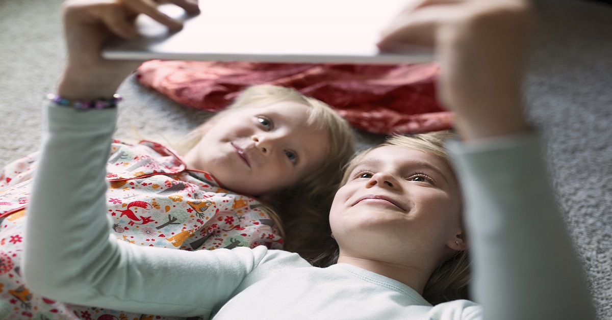 Smiling sisters lying on the floor taking selfie with digital tablet
