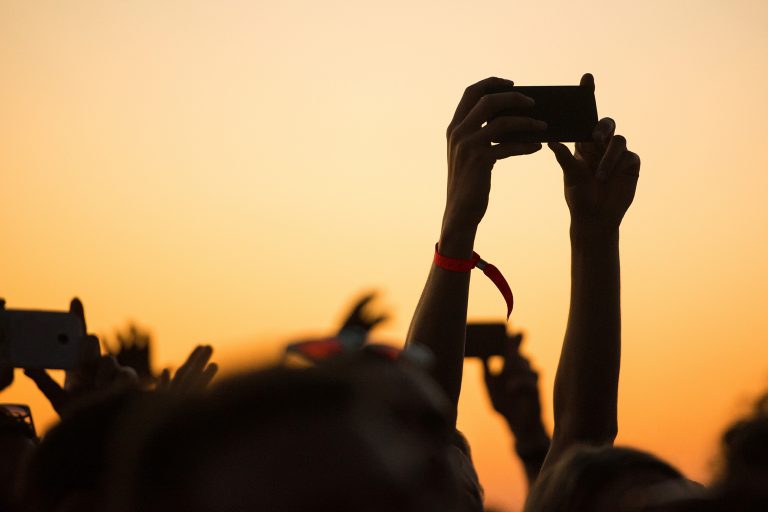Sunset image showing people's hands in the air, filming and taking photos