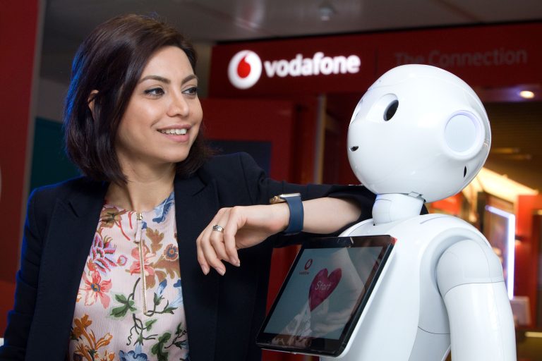 Photo of Vodafone UK's Samira Maleki, Operational Governance & Transformation Manager, pictured with Pepper the humanoid robot in front of a Vodafone store