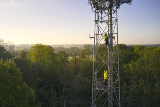 Engineers climbing up a telecoms mast in UK countryside.