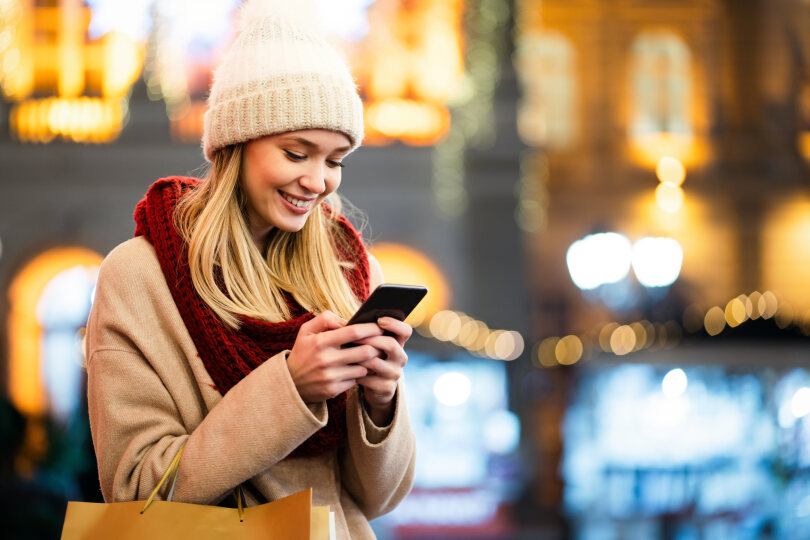 Portrait of smiling woman using mobile phone in the city at winter, using mobile phone.