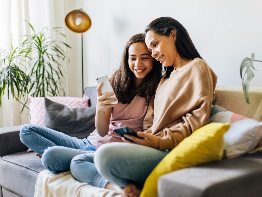 Mother and daughter sat on sofa looking at smartphones.