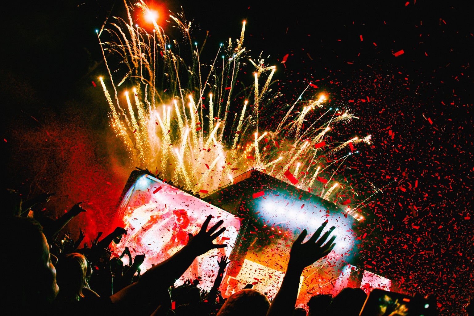 Hands in air in festival crowd, with fireworks in the background.