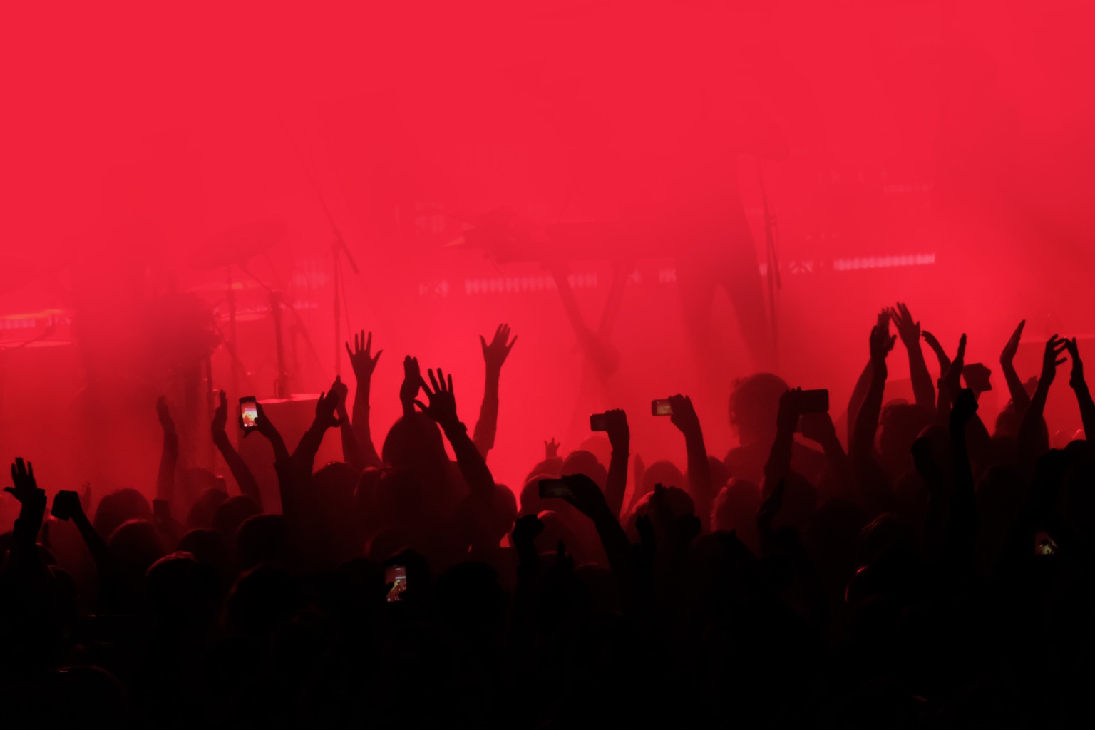 Silhouette of fans' hand waving at live music gig, with red background.