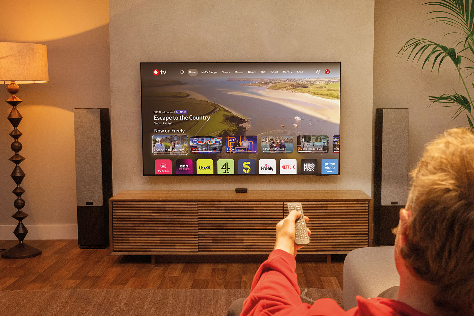 lifestyle shot of man pointing remote control at Vodafone TV while seated in a living room lifestyle shot of man pointing remote control at Vodafone TV while seated in a living room