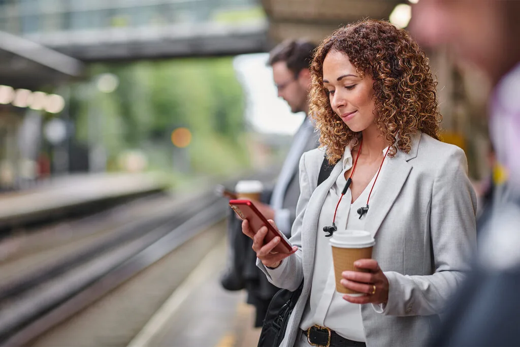 woman using red smartphone while waiting on a train station platform
