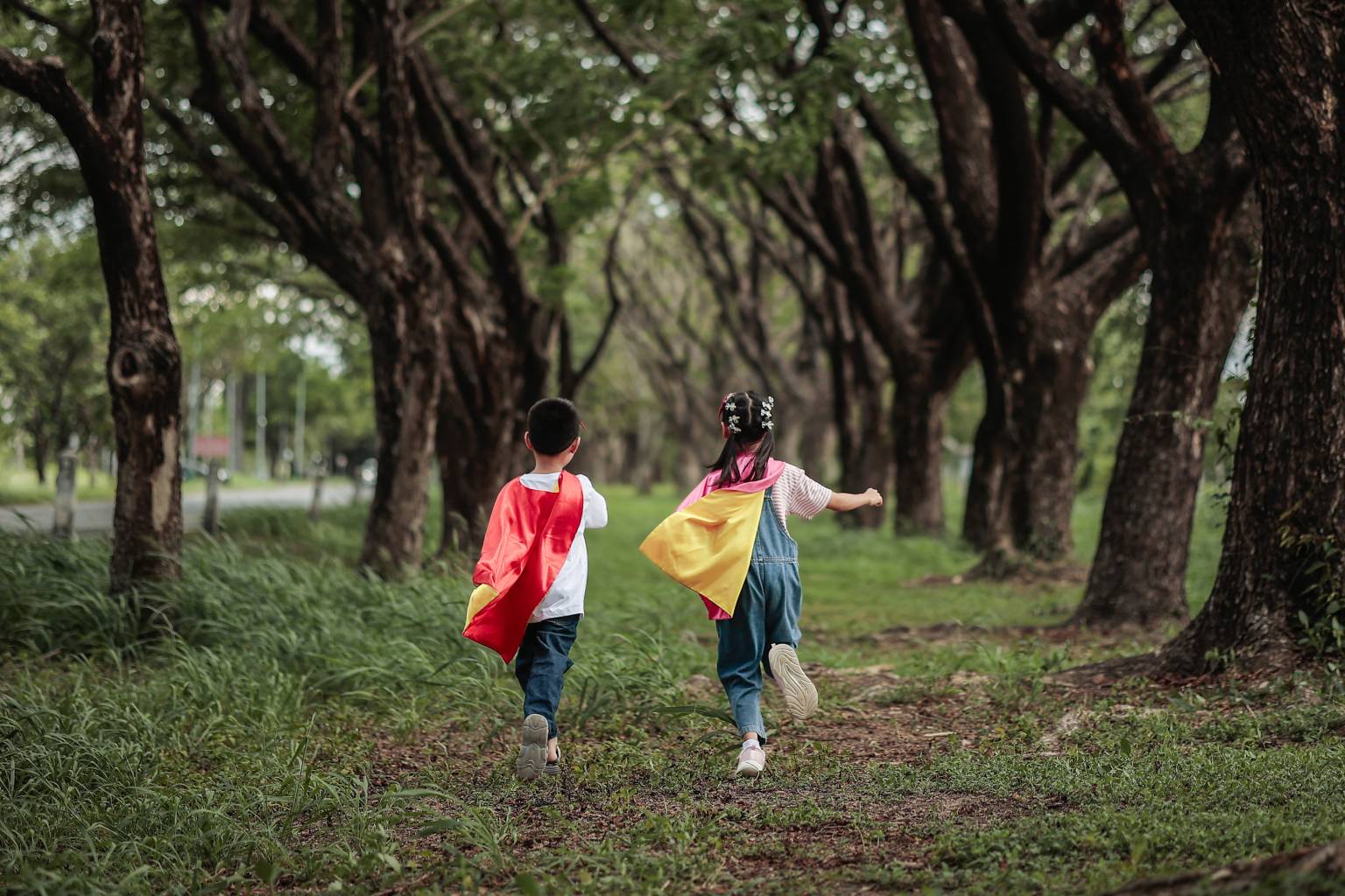 Two children running through forest, wearing capes.